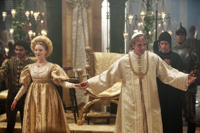 Actors Holliday Grainger and Jeremy Irons stand with arms spread, holding hands, acting as Lucrezia Borgia and her father, Pope Alexander VI.