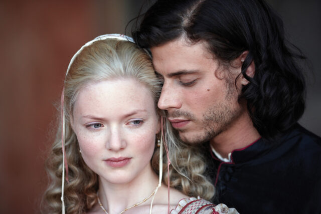 Actors Holliday Grainger and Francois Arnaud playing Lucrezia and Cesare Borgia, his face very close to hers from behind.