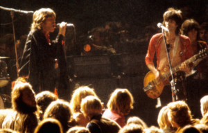 The Rolling Stones performing on stage, heads of the crowd visible.