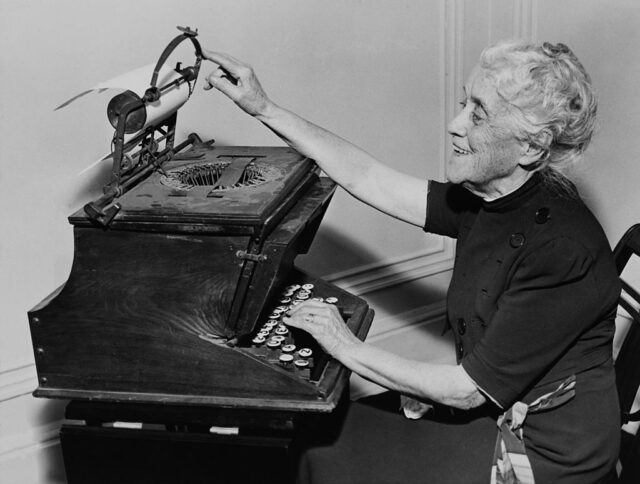 Elderly woman working away at an old typewriter. 