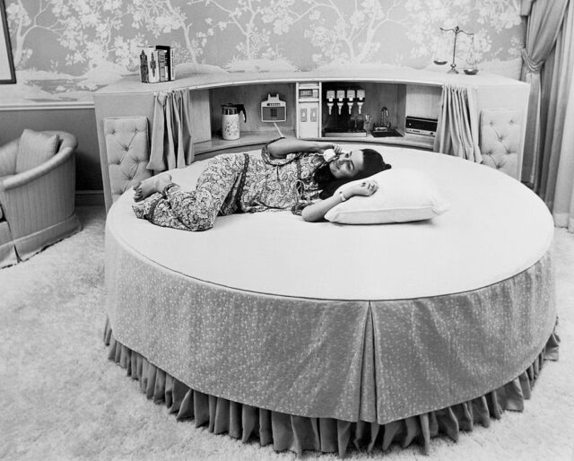 Woman lying on a circular bed while talking on the phone.