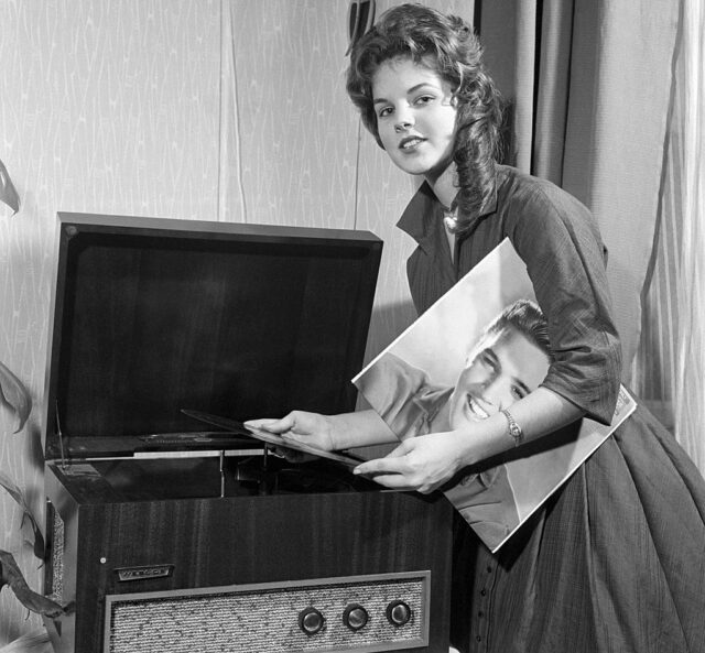 Woman putting a vinyl record on, while holding the cover with Elvis Presley's face on it.