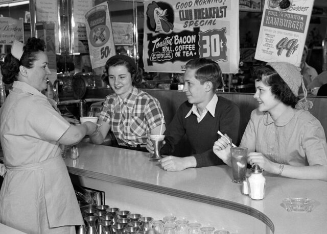 Woman serving three children sitting at the front table of a diner