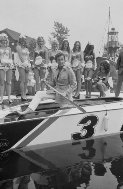 Bob Guccione rowing a boat past a group of Penthouse models