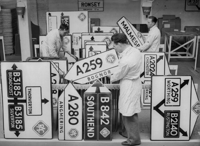 Three men standing with numerous road signs