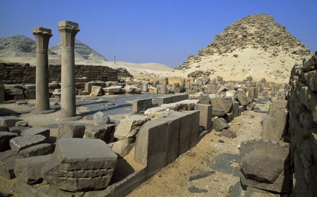 A pyramid with several stone debris pieces in front, along with two stone columns.