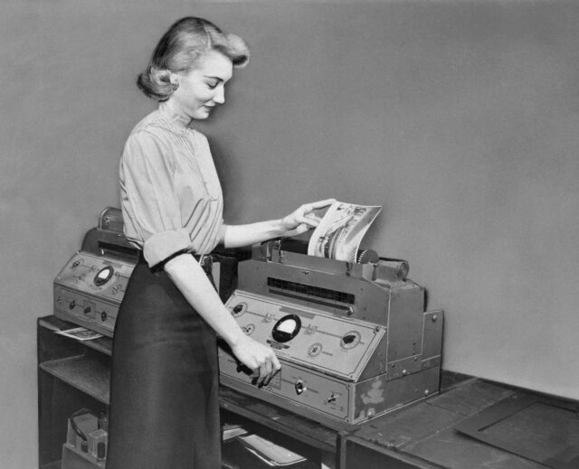 A woman working an old fax machine.