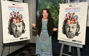Kelly Carlin standing between two poster boards with George Carlin's face on them
