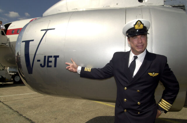 John Travolta in a pilots uniform standing in front of a small aircraft.