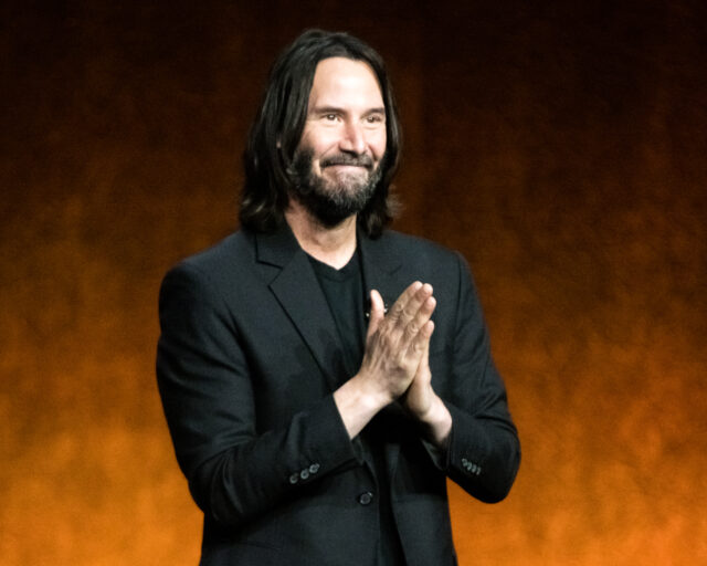 Keanu Reeves with his hands together in front of him in thanks.