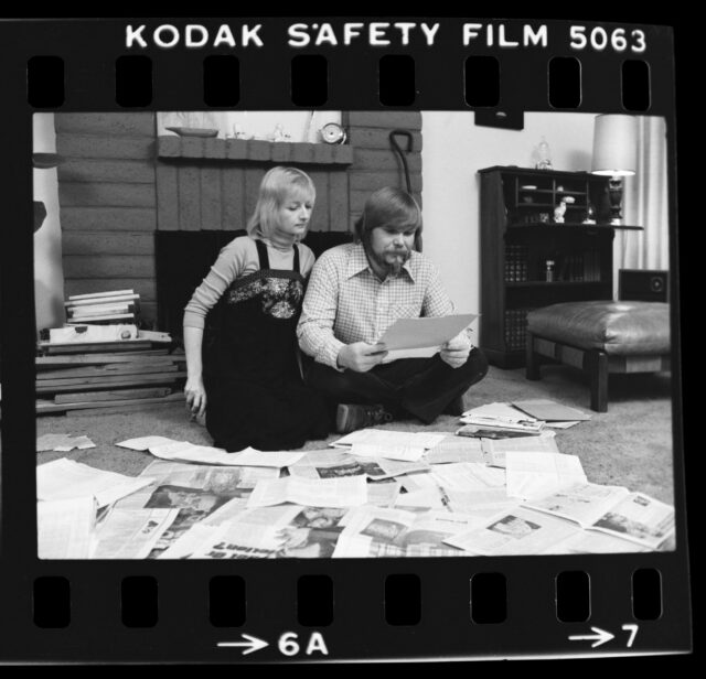 George Lee and Kathleen Lutz sitting on the floor, surrounded by newspapers.