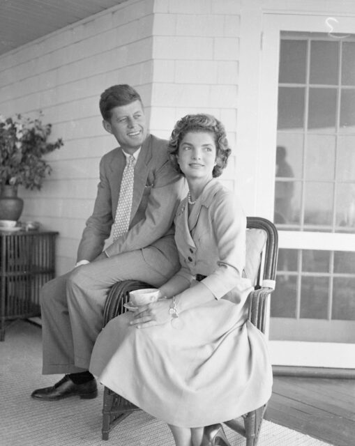 Jacqueline Bouvier and John F. Kennedy sitting on a chair together.