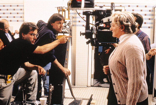 Chris Columbus and Robin Williams, dressed as Mrs. Doubtfire, behind the scenes. A camera sits between them.