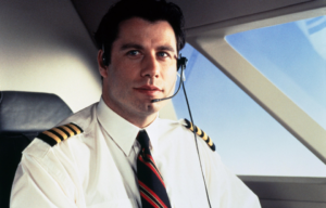 John Travolta in a pilot uniform sitting in a cockpit.