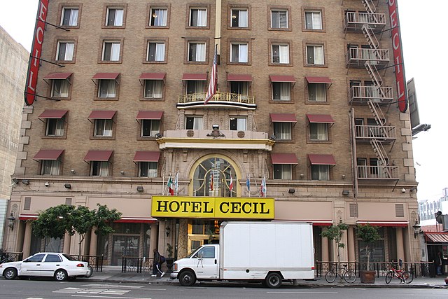 Car and white truck parked outside of the Cecil Hotel