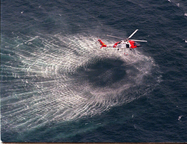 A helicopter flying over water, waves caused by its turbine.
