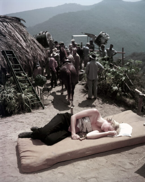 Grace Kelly lying on a mattress, people with horses walking away.
