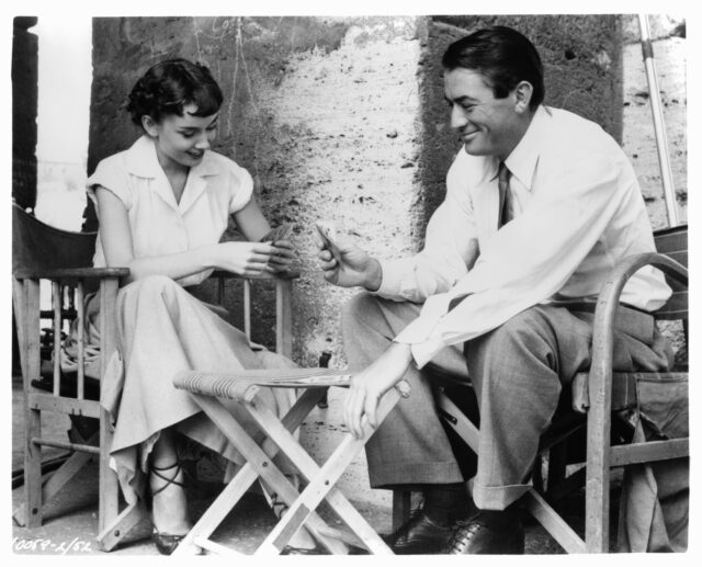 Audrey Hepburn and Gregory Peck sitting and playing cards.