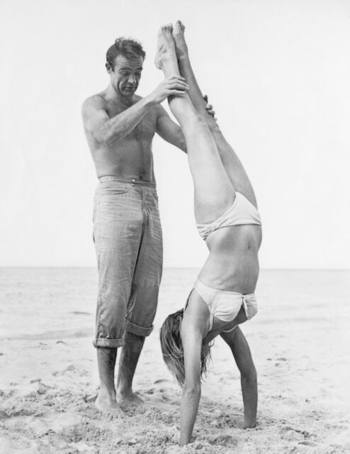 Sean Connery holds Ursula Andress' ankles as she does a handstand.