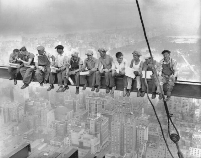 Steelworkers eating their lunch on a steel beam high in the sky.