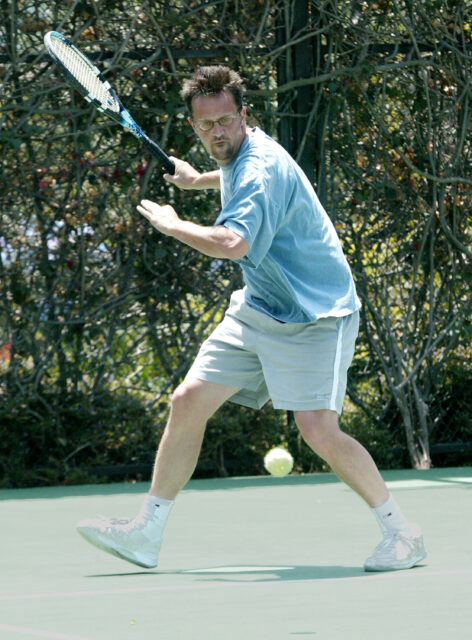 Matthew Perry about to hit a tennis ball on the court