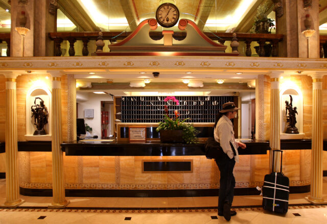 Man standing at the front desk of the Cecil Hotel with a suitcase