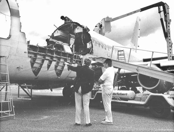 Two men inspect the damage of a commercial airplane missing part of its fuselage roof.