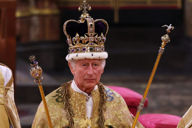 King Charles III wearing his crown and holding two sceptres. 