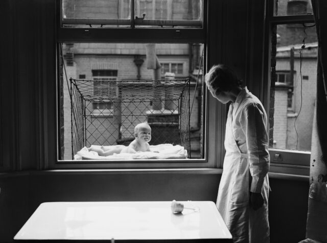 A woman looks at her baby in a cage out the window.