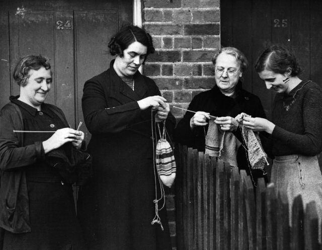 Four women standing around, knitting.