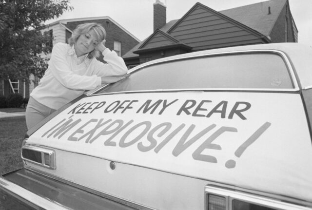 A woman leaning on the rear of her car.