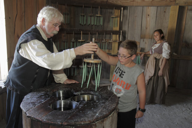 An older man showing a young boy how to dip candles.