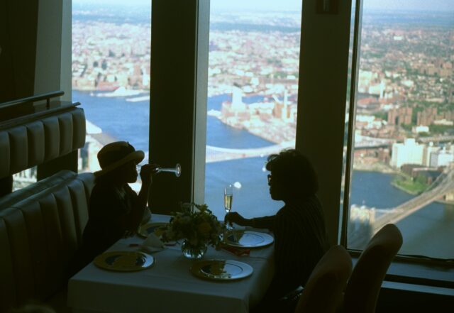 A table of two dinning at the Window of the World flanked by the city views through vertical windows.