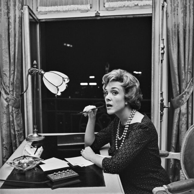 Micheline Presle holding a pen near her mouth while sitting at a writing desk