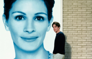 Hugh Grant walking in front of a poster of Julia Roberts.