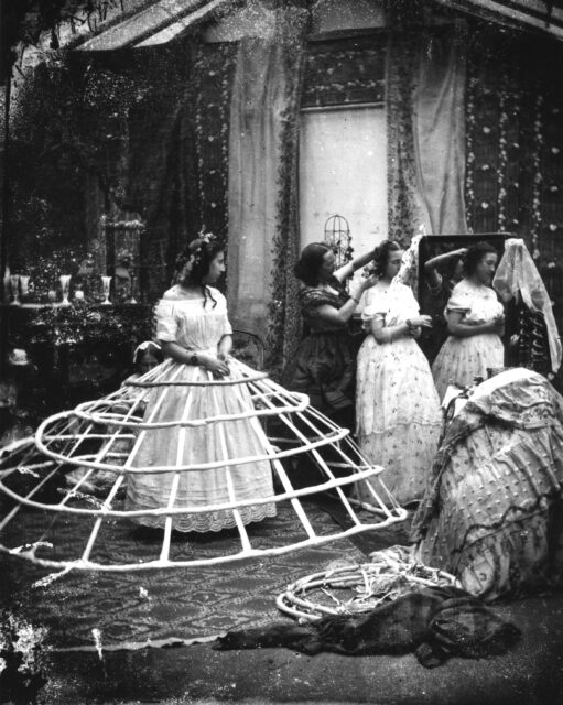 A woman being dressed, wearing a crinoline.