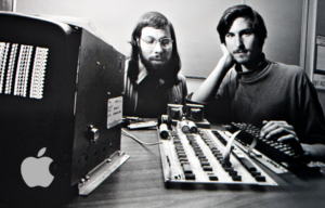 Young Steve Jobs and Steve Wozniak sitting at a desk with tech gear in front of them.