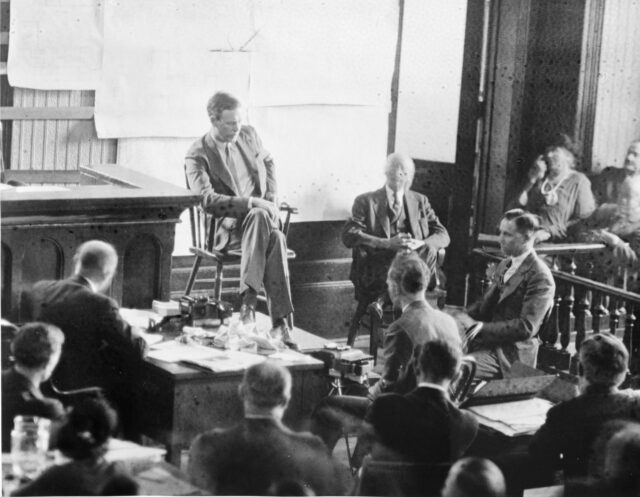 A man sitting on trial surrounded by other men.