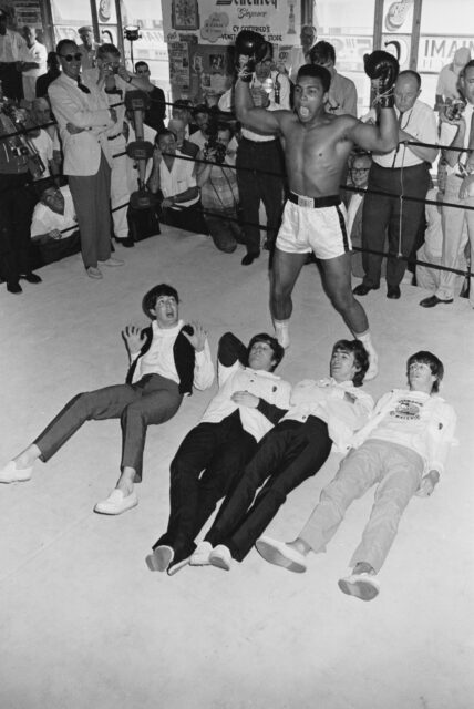 The Beatles lay on the ground in front of Muhammad Ali.