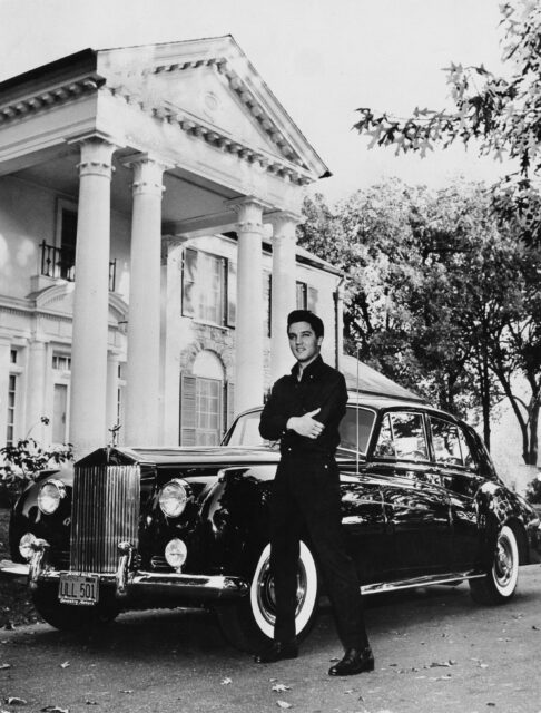 Elvis standing in front of a car in front of Graceland.