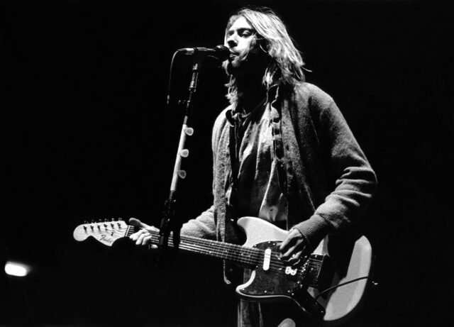 kurt cobain onstage playing the guitar, singing into microphone