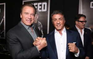 Arnold Schwarzenegger and Sylvester Stallone clasping hands for a photo.