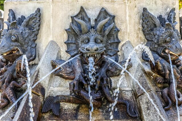 Demon sculptures on a fountain with water pouring from their mouths.