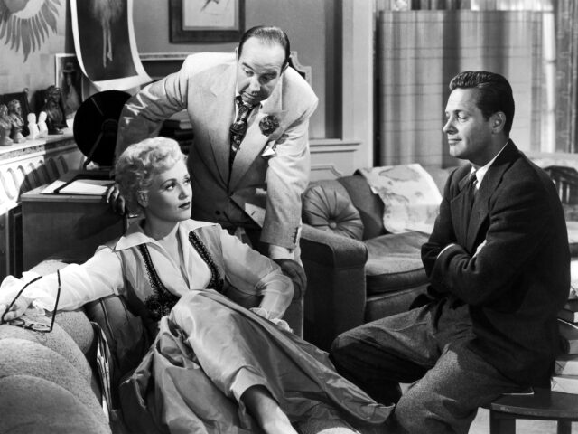 Judy Holliday sitting on a couch with two men around her in "Born Yesterday."