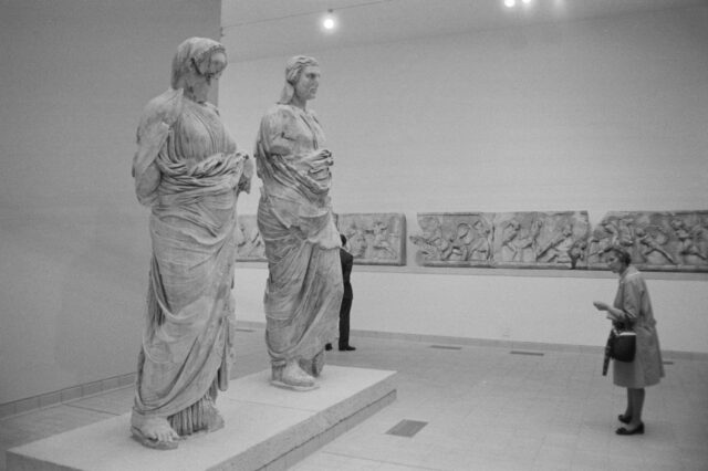 A woman looks at two ancient sculptures in a museum. 