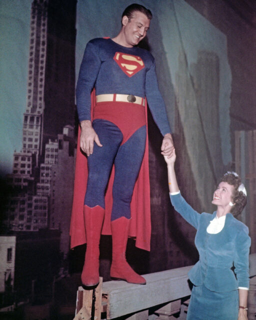 George Reeves stands on a riser holding hands with Phyllis Coates.