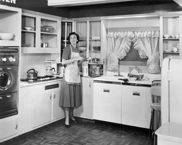 A woman stands in a fully equipped kitchen.