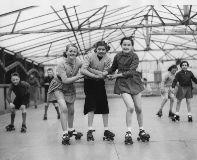Three girls hold hands while roller skating.