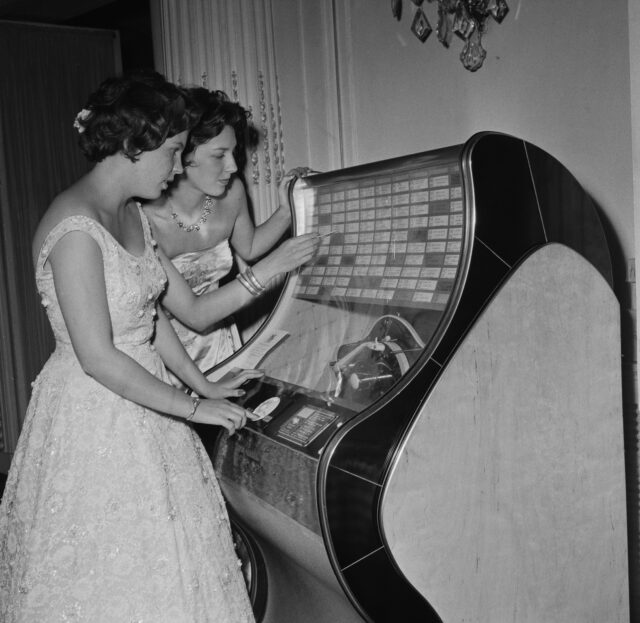 Two girls search for a song on a jukebox.