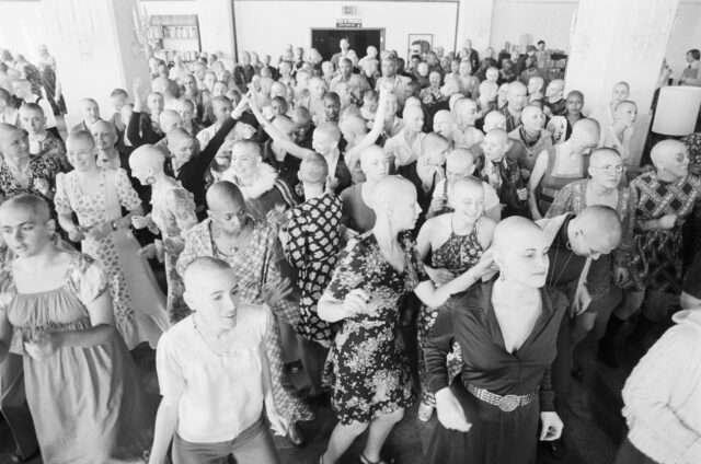Women with shaved heads dancing in a room.